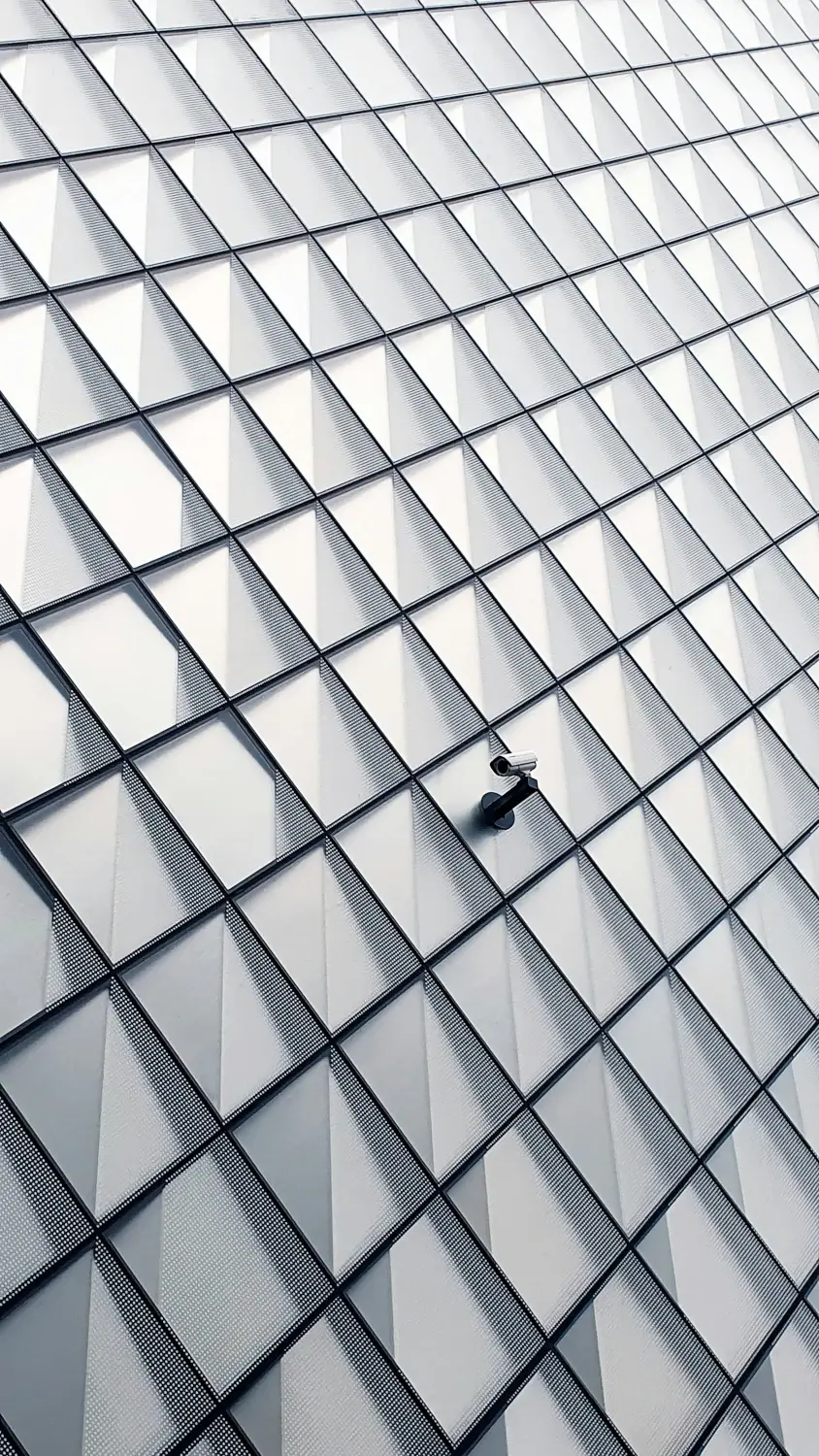 Une caméra de surveillance au milieu d'une façade en verre. En logiciel la sécurité est un point d'attention important pour éviter les failles de sécurité